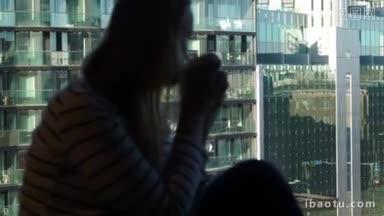 多利拍摄的一个女人喝咖啡坐在窗口与城市景观现代玻璃<strong>建筑</strong>闪闪<strong>发光</strong>